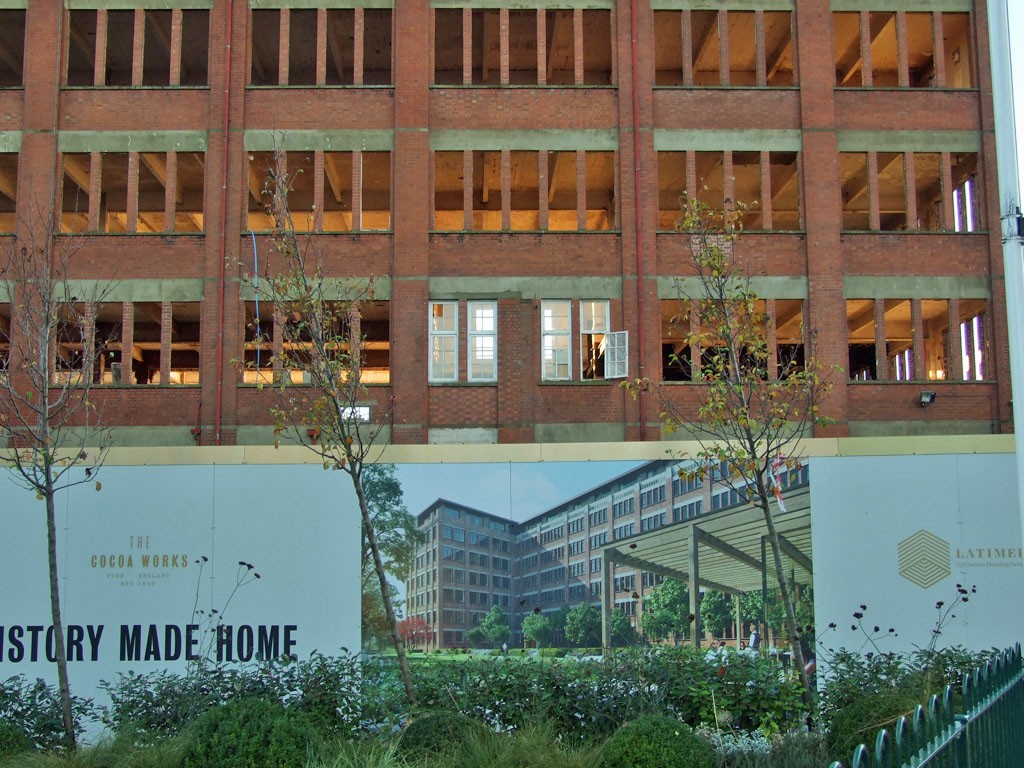 Shell of old factory building with hoardings below showing images of how it will look