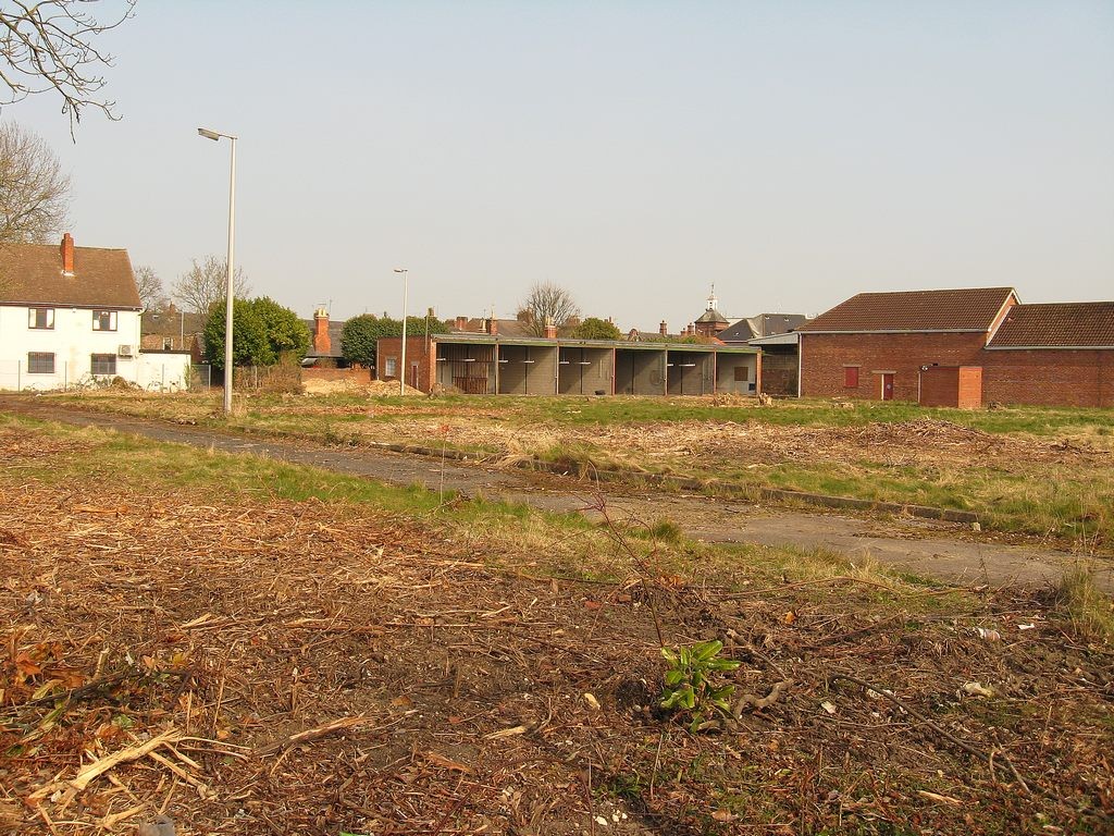 Grassed cleared site with small buildings remaining