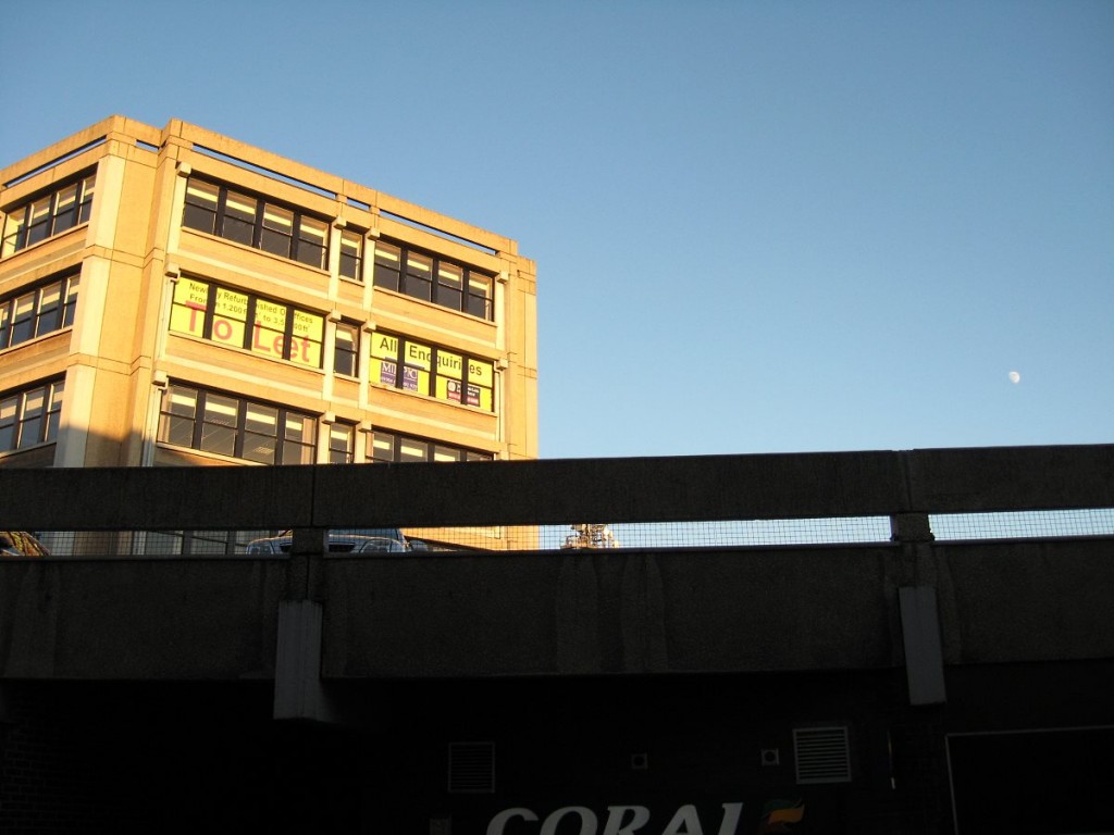 Concrete building lit by sun, dark parapet in foreground, blue sky behind