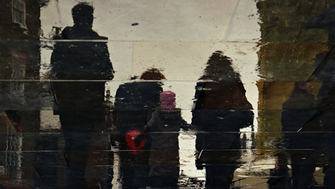 People walking, reflecting in wet paving